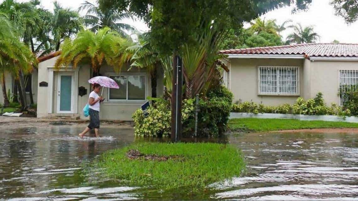 photo: woman walking on flooded sidewalk in Florida. Three newspapers confront one challenge: Sea-level rise is real, South Florida needs all hands on deck — now